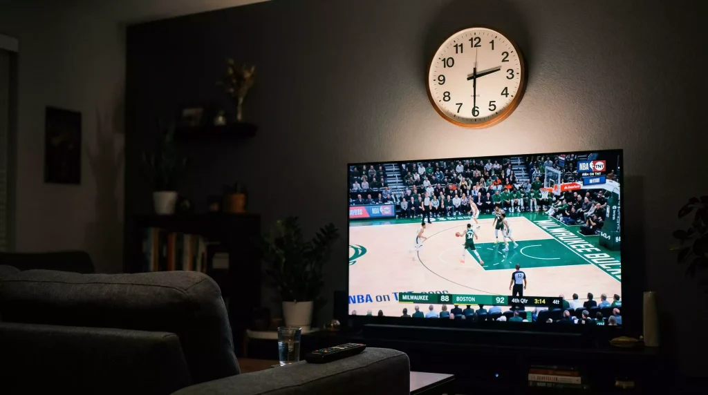 Reloj de pared mostrando la madrugada con un televisor encendido al fondo en un salón